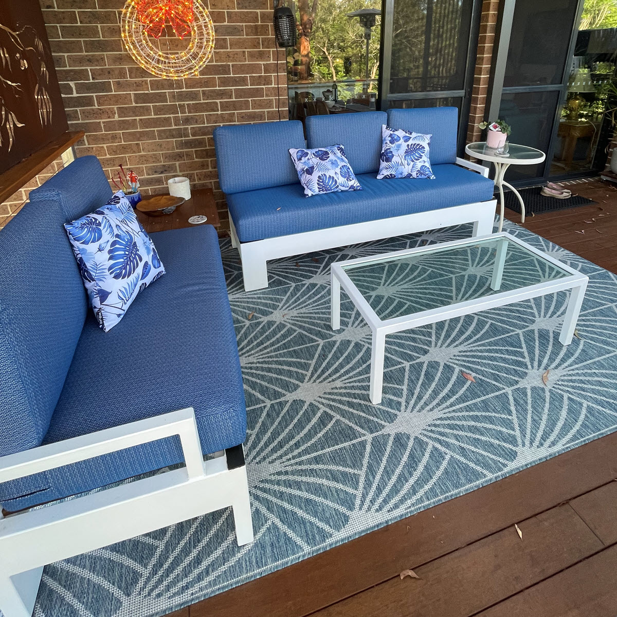 Blue patio furniture cushions with floral pattern throw pillows on wooden decking.